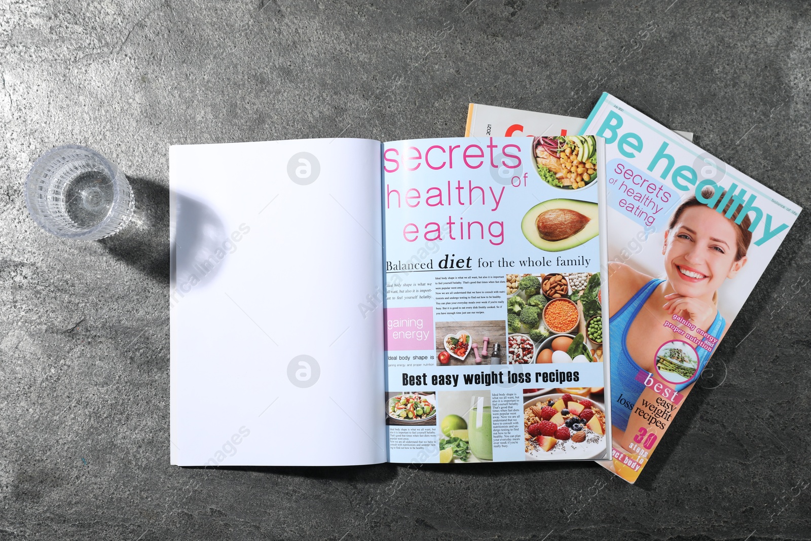 Trendy magazines and glass of water on grey background, top view. Mockup for design Photo of Trendy magazines and glass of water on grey background, top view. Mockup for design