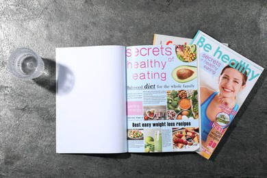 Photo of Trendy magazines and glass of water on grey background, top view. Mockup for design