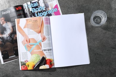 Photo of Trendy magazines and glass of water on grey background, top view. Mockup for design