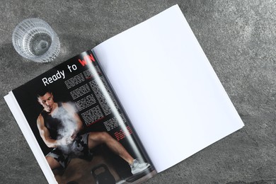 Photo of Open magazine and glass of water on grey background, top view. Mockup for design