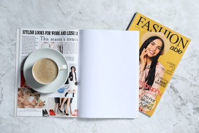 Photo of Trendy magazines and cup of coffee on white marble background, top view. Mockup for design