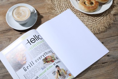 Photo of Open magazine, pretzels and coffee on wooden background, closeup. Mockup for design
