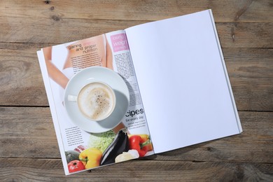 Photo of Open magazine and coffee on wooden background, top view. Mockup for design
