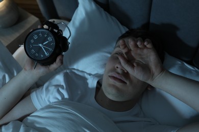 Photo of Frustrated man with alarm clock suffering from insomnia in bed indoors, above view