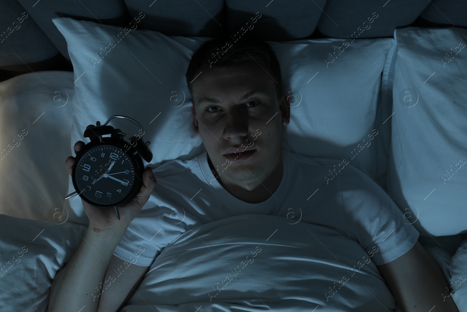 Photo of Frustrated man with alarm clock suffering from insomnia in bed indoors, top view