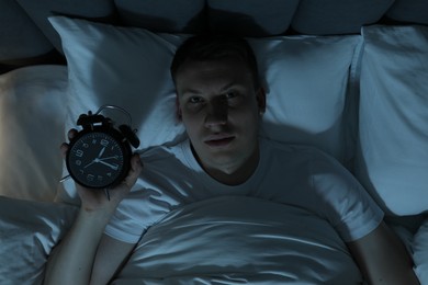Photo of Frustrated man with alarm clock suffering from insomnia in bed indoors, top view