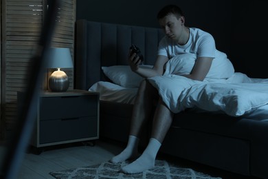 Photo of Frustrated man with alarm clock suffering from insomnia on bed indoors