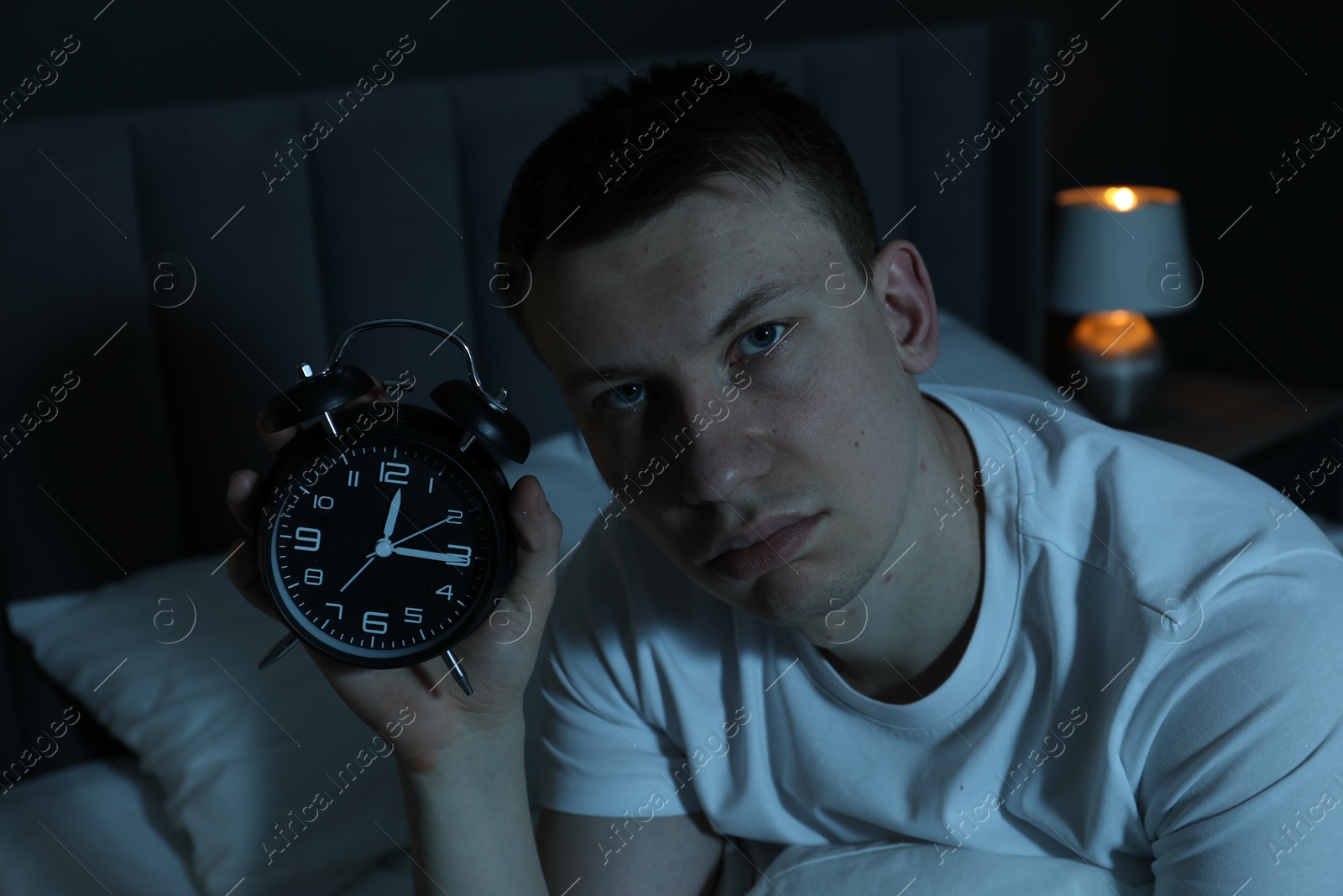 Frustrated man with alarm clock suffering from insomnia on bed indoors Photo of Frustrated man with alarm clock suffering from insomnia on bed indoors