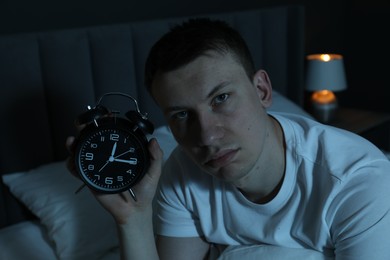 Photo of Frustrated man with alarm clock suffering from insomnia on bed indoors