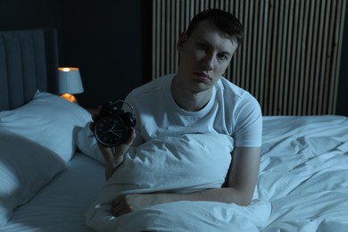 Photo of Frustrated man with alarm clock suffering from insomnia on bed indoors