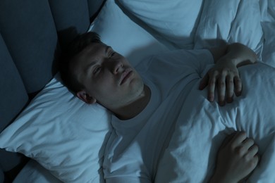 Photo of Frustrated man suffering from insomnia in bed indoors, above view