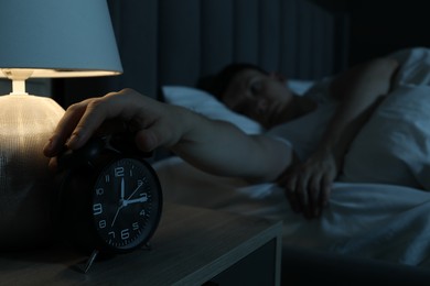 Photo of Frustrated man suffering from insomnia in bed indoors, focus on alarm clock