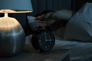 Photo of Man suffering from insomnia in bed indoors, focus on alarm clock