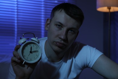 Photo of Frustrated man with alarm clock suffering from insomnia indoors