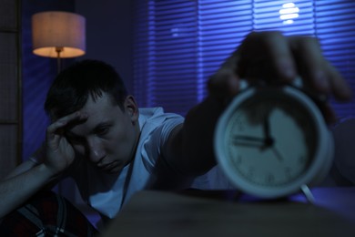 Photo of Frustrated man suffering from insomnia and turning off alarm clock indoors, selective focus