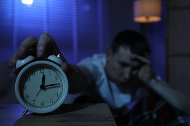 Photo of Frustrated man suffering from insomnia indoors, focus on alarm clock