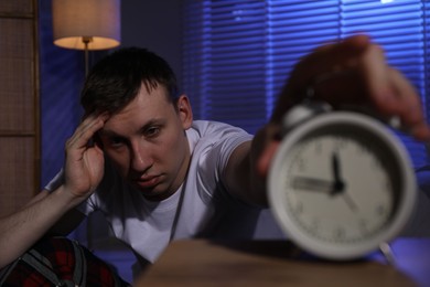 Photo of Frustrated man suffering from insomnia and turning off alarm clock indoors, selective focus