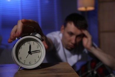 Photo of Frustrated man suffering from insomnia and turning off alarm clock indoors, selective focus