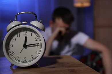 Photo of Frustrated man suffering from insomnia indoors, focus on alarm clock