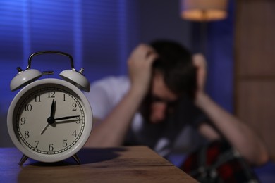 Photo of Frustrated man suffering from insomnia indoors, focus on alarm clock