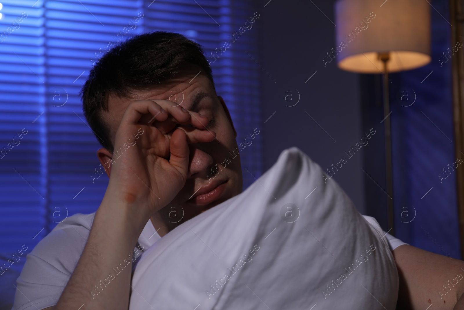Photo of Frustrated man with pillow suffering from insomnia indoors