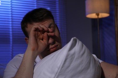 Photo of Frustrated man with pillow suffering from insomnia indoors