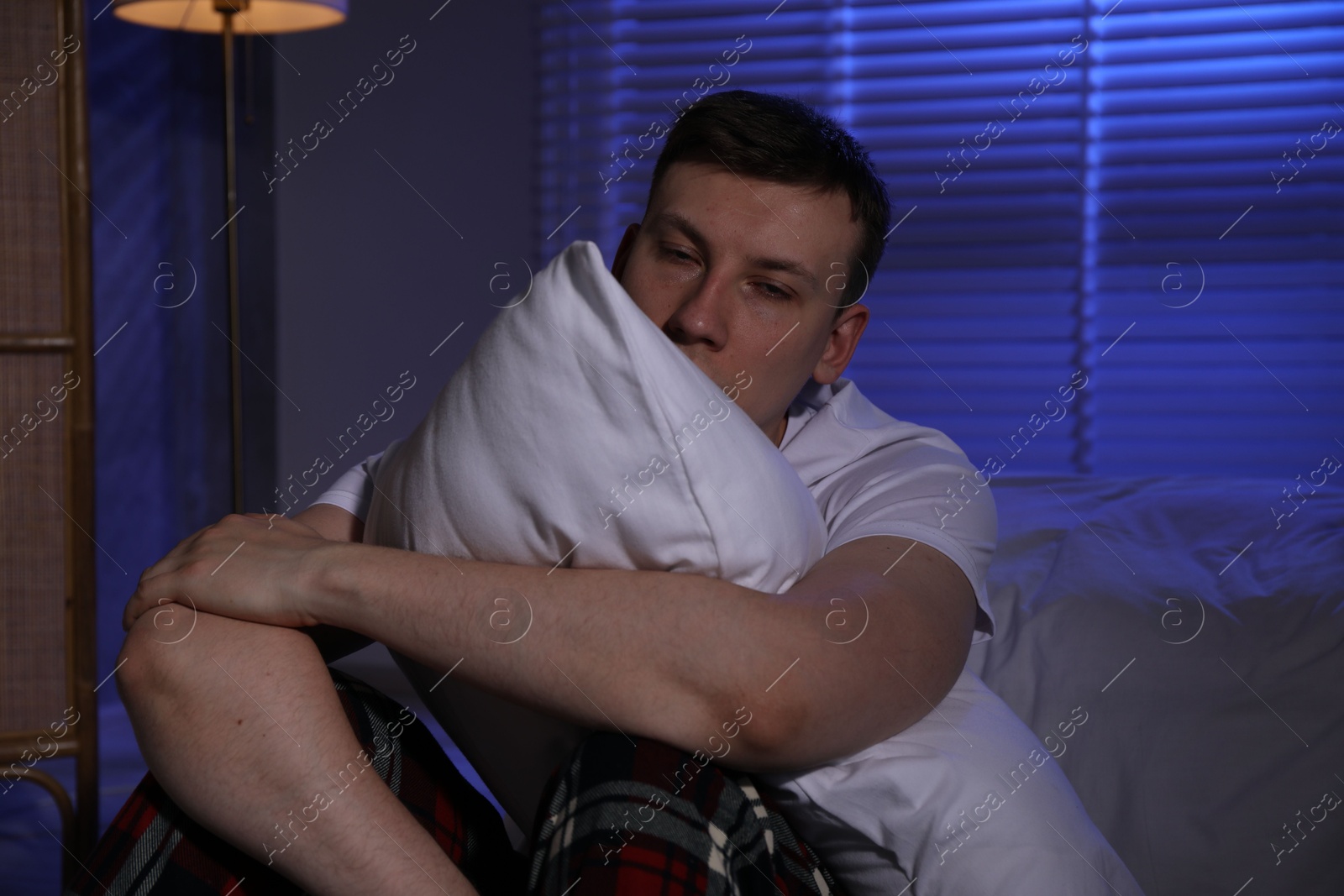 Frustrated man with pillow suffering from insomnia on floor indoors Photo of Frustrated man with pillow suffering from insomnia on floor indoors