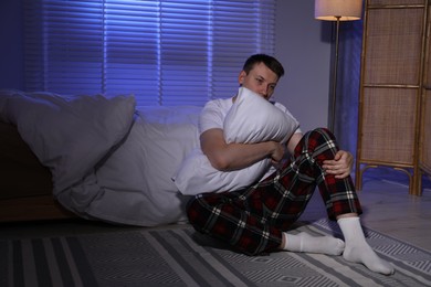 Photo of Frustrated man with pillow suffering from insomnia on floor indoors