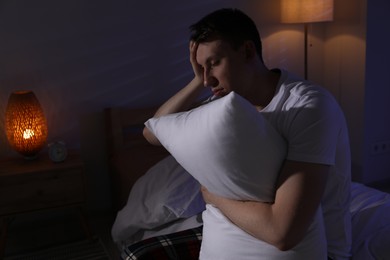 Photo of Frustrated man with pillow suffering from insomnia on bed indoors, space for text
