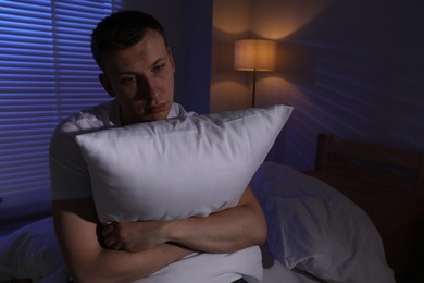 Photo of Frustrated man with pillow suffering from insomnia on bed indoors