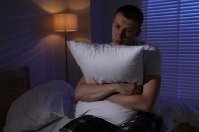 Photo of Frustrated man with pillow suffering from insomnia on bed indoors