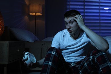 Photo of Frustrated man with alarm clock suffering from insomnia on floor indoors