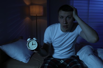 Photo of Frustrated man with alarm clock suffering from insomnia on bed indoors