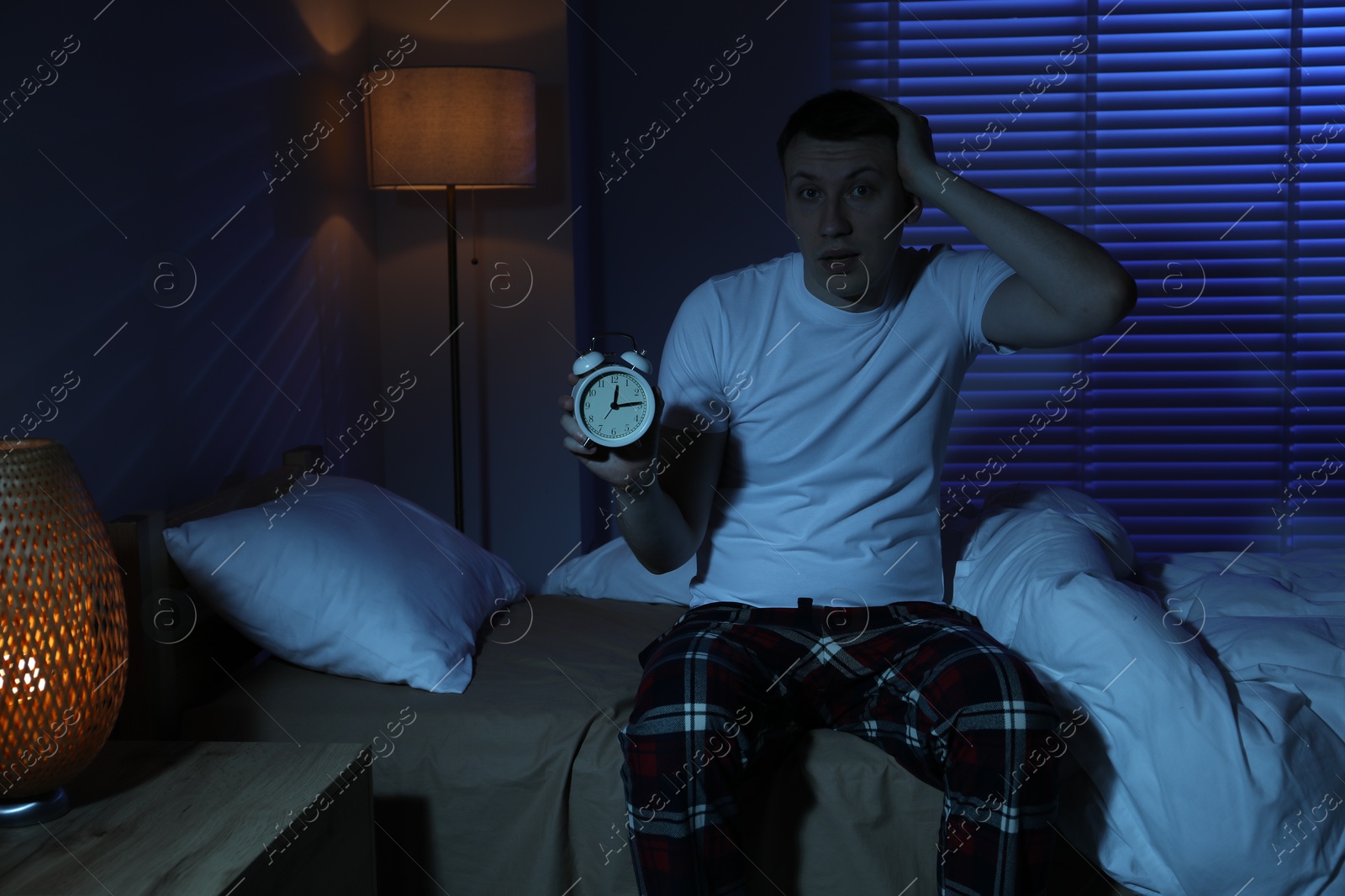 Frustrated man with alarm clock suffering from insomnia on bed indoors Photo of Frustrated man with alarm clock suffering from insomnia on bed indoors