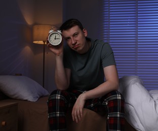 Photo of Frustrated man with alarm clock suffering from insomnia on bed indoors