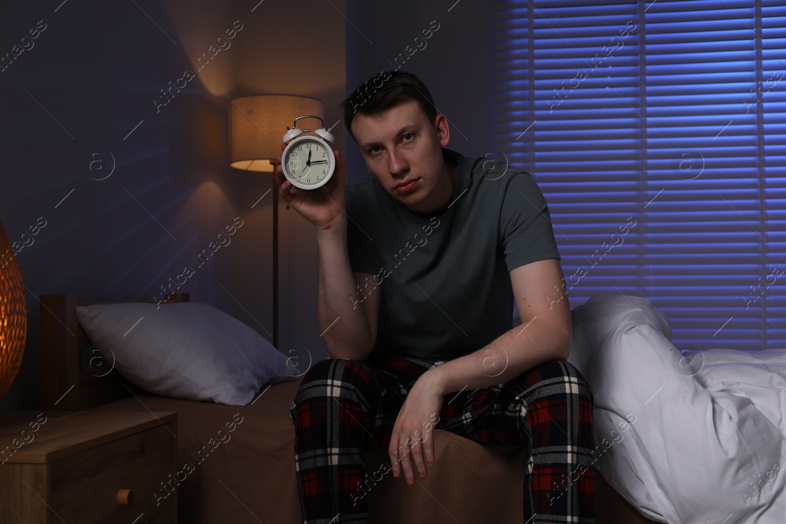 Photo of Frustrated man with alarm clock suffering from insomnia on bed indoors