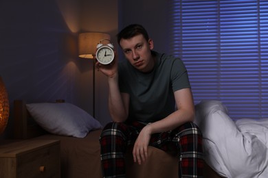 Photo of Frustrated man with alarm clock suffering from insomnia on bed indoors