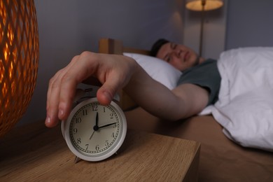 Photo of Frustrated man suffering from insomnia and turning off alarm clock in bed indoors, selective focus