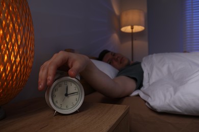 Photo of Frustrated man suffering from insomnia and turning off alarm clock in bed indoors, selective focus