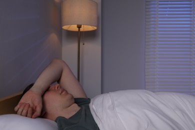 Photo of Frustrated man with alarm clock suffering from insomnia in bed indoors