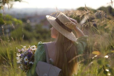 Photo of Woman with beautiful wildflowers, hat and backpack in meadow on sunny day, back view