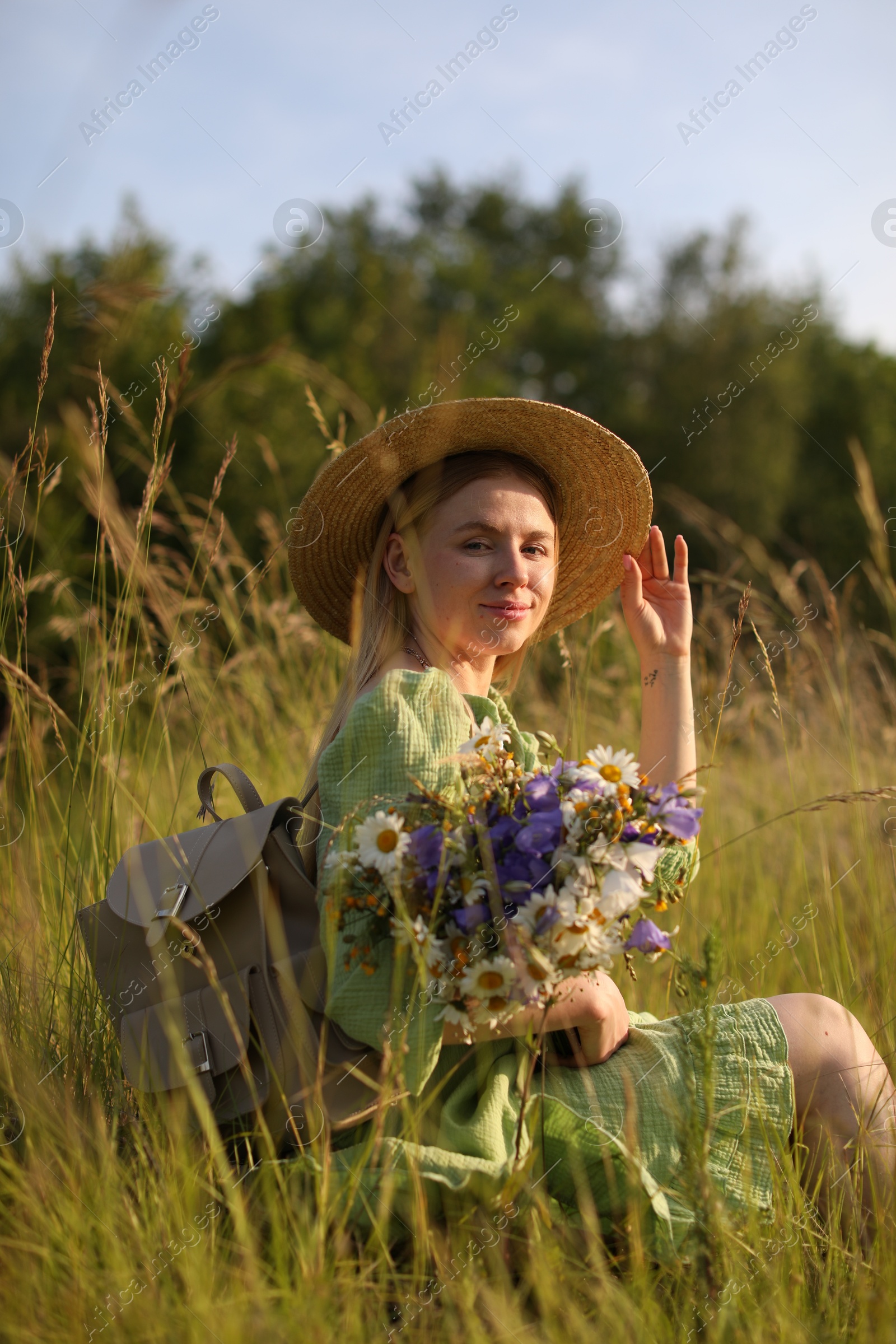 Woman with beautiful wildflowers, hat and backpack in meadow on sunny day Photo of Woman with beautiful wildflowers, hat and backpack in meadow on sunny day