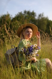 Photo of Woman with beautiful wildflowers, hat and backpack in meadow on sunny day