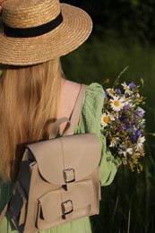 Photo of Woman with beautiful wildflowers, hat and backpack in meadow on sunny day, back view
