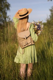 Photo of Woman with beautiful wildflowers, hat and backpack in meadow on sunny day, back view