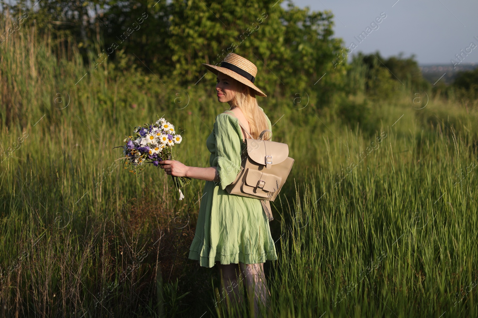 Woman with beautiful wildflowers, hat and backpack in meadow on sunny day Photo of Woman with beautiful wildflowers, hat and backpack in meadow on sunny day