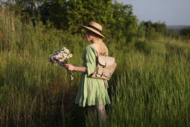 Photo of Woman with beautiful wildflowers, hat and backpack in meadow on sunny day