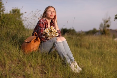 Photo of Beautiful woman with wildflowers and backpack enjoying summer day in meadow. Space for text
