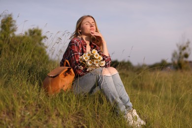 Photo of Beautiful woman with wildflowers and backpack enjoying summer day in meadow
