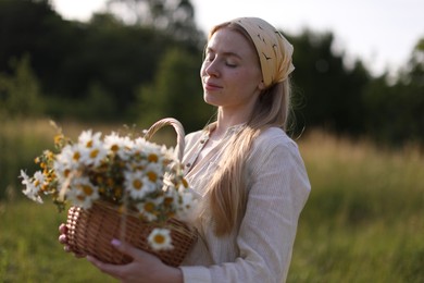 Photo of Happy woman with basket full of beautiful wildflowers outdoors